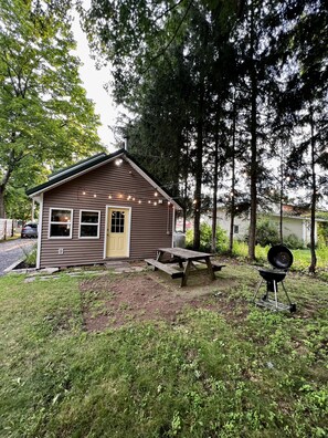 Une petite cabane avec une façade en bois, une porte d’entrée et une table de pique-nique devant.