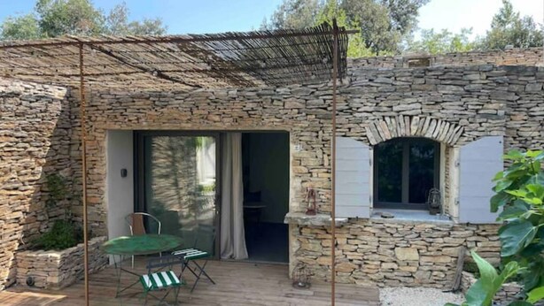 Un bâtiment en pierre doté d’un patio, d’une table avec des chaises et d’une fenêtre avec des volets.