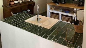Une cuisine avec un plan de travail recouvert de carreaux verts, des meubles en bois et des luminaires suspendus.