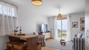 Ein modernes Wohnzimmer mit Esstisch aus Holz, gestreifter Couch und einem Fernseher.