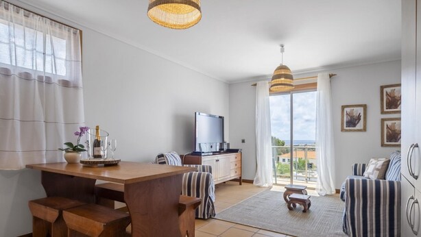 A modern living room with a wooden dining table, striped sofa, and a television. - Casa Anaim by Homie in Porto Santo (Porto Santo)