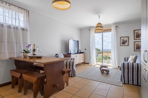 Ein modernes Wohnzimmer mit Esstisch aus Holz, gestreifter Couch und einem Fernseher.
