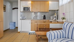 Eine kleine Küche mit Mikrowelle, Toaster und Kaffeemaschine. Im Wohnbereich befindet sich eine Holzbank und ein gestreiftes Sofa.