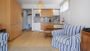 A compact kitchen with wooden cabinets, a microwave, and a sink. There is a striped sofa and a small table in the living area. - Casa Anaim by Homie in Porto Santo (Porto Santo)