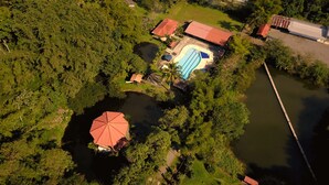 An aerial view of a property with a swimming pool, a tennis court, and a large red-roofed pavilion.