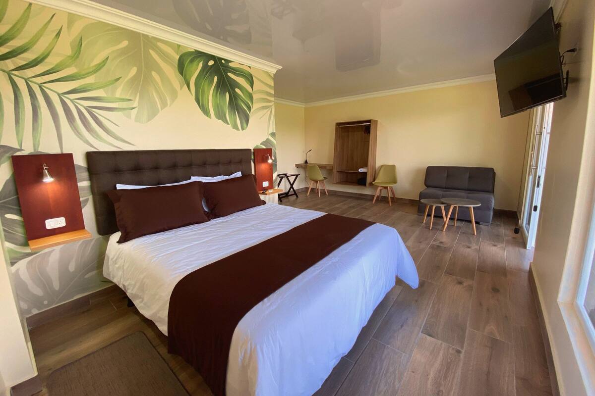 Une chambre d’hôtel avec un grand lit, une télévision, un coin salon avec un canapé et des fauteuils, et un plancher en bois.