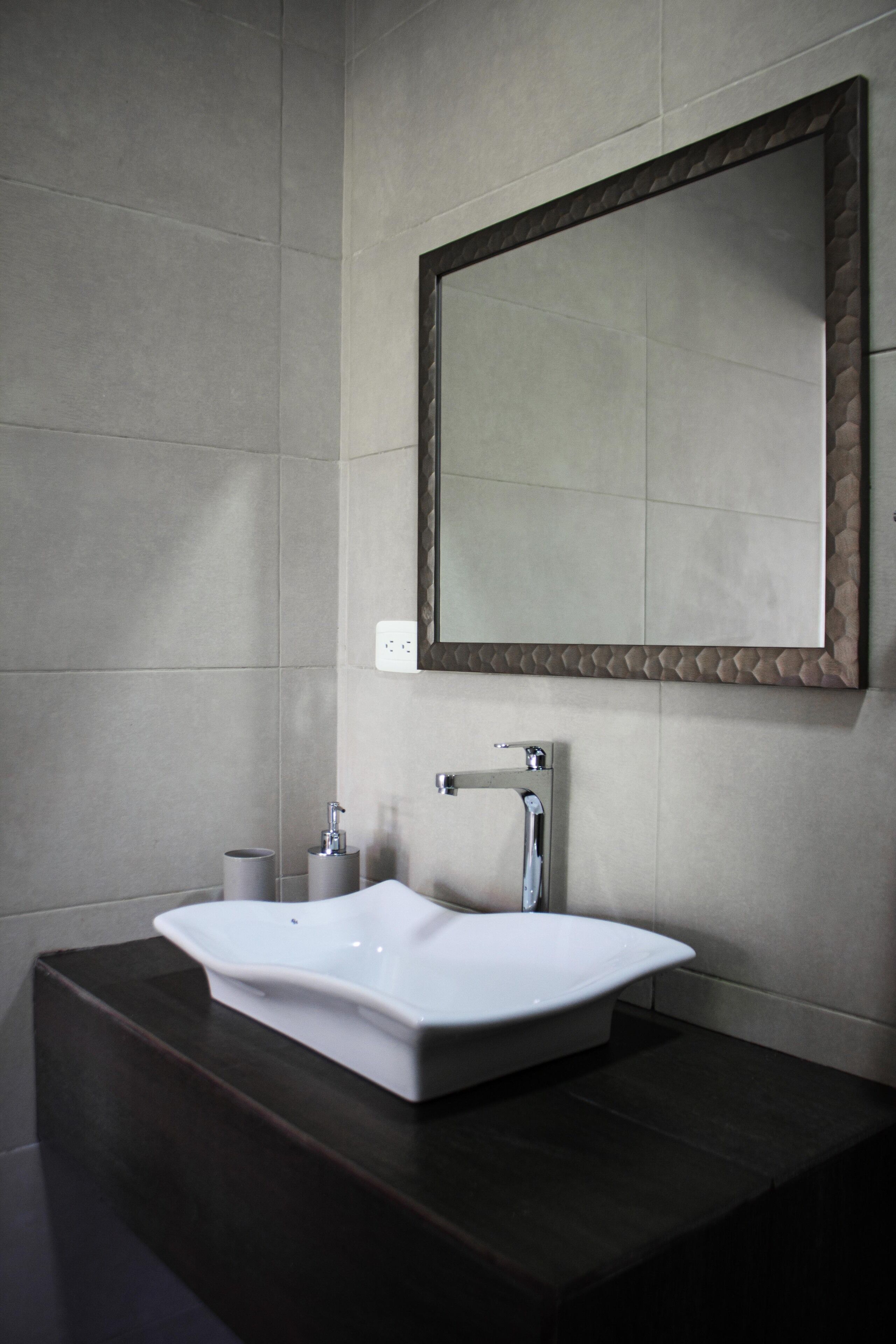 Une salle de bain avec un grand miroir, un lavabo blanc et un plan de toilette foncé.
