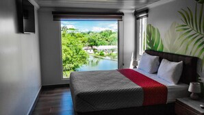A bedroom with a large bed, a view of a lake, and a tropical plant on the wall.