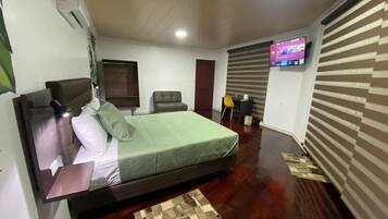 Un dormitorio con cama, escritorio, silla, televisión y ventana.