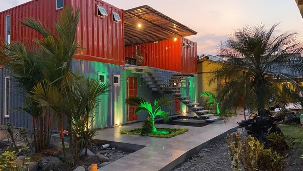 A modern house with a red and blue exterior, a staircase, and a small garden with palm trees.