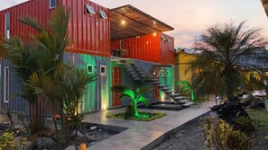 Una casa moderna con fachada roja y azul, una escalera y un pequeño jardín con palmeras.