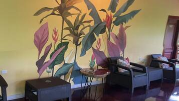 A room with a large wall mural of tropical plants, a round table with a glass, and two wicker sofas.