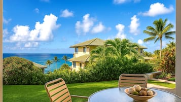 A beachfront property with a two-story house, a well-maintained lawn, and a dining area with a table and chairs.