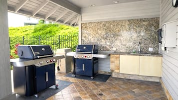 An outdoor kitchen area with two barbecue grills, a granite countertop, and a sink.