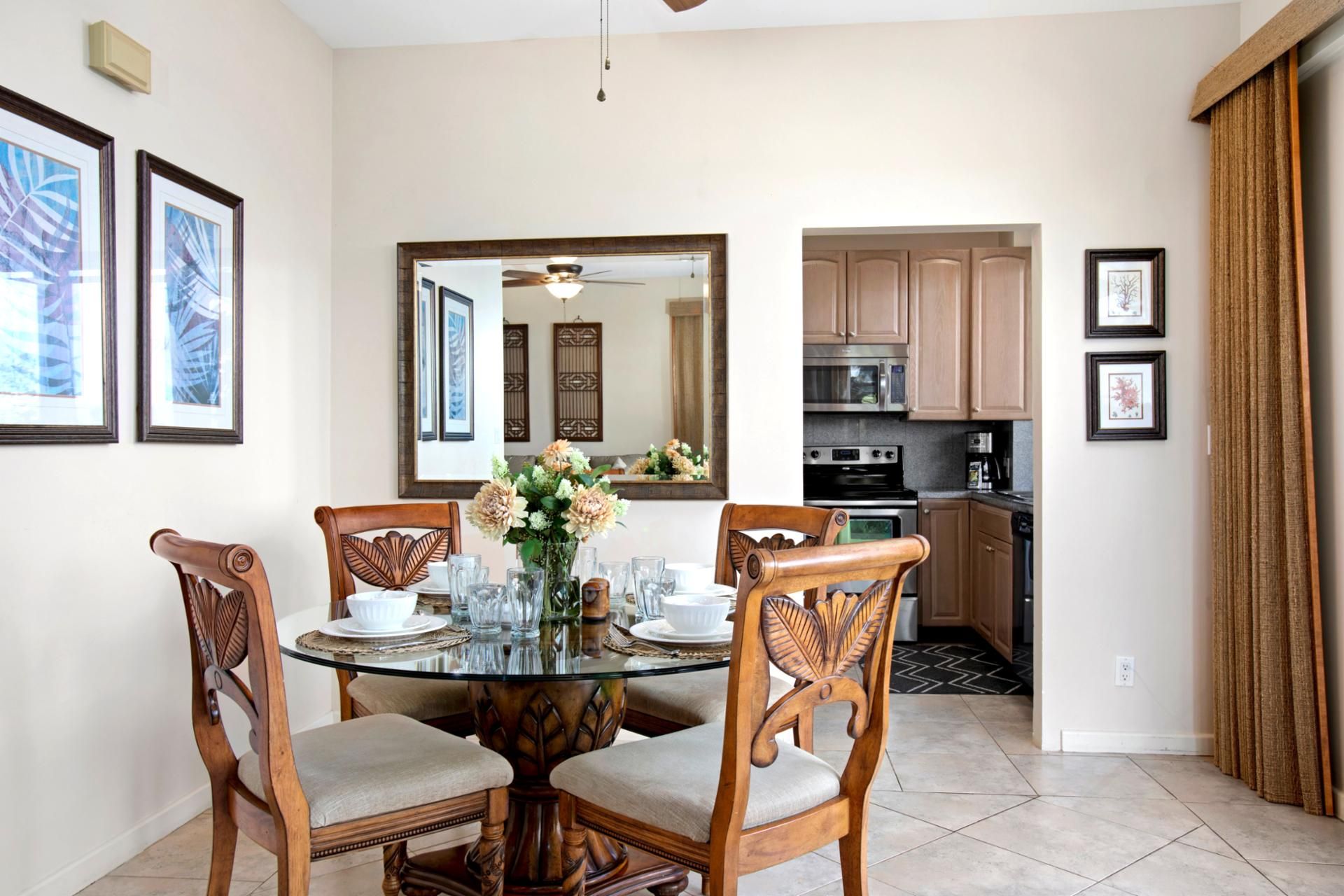A dining area with a round table, four wooden chairs, a vase with flowers, and framed pictures on the wall.