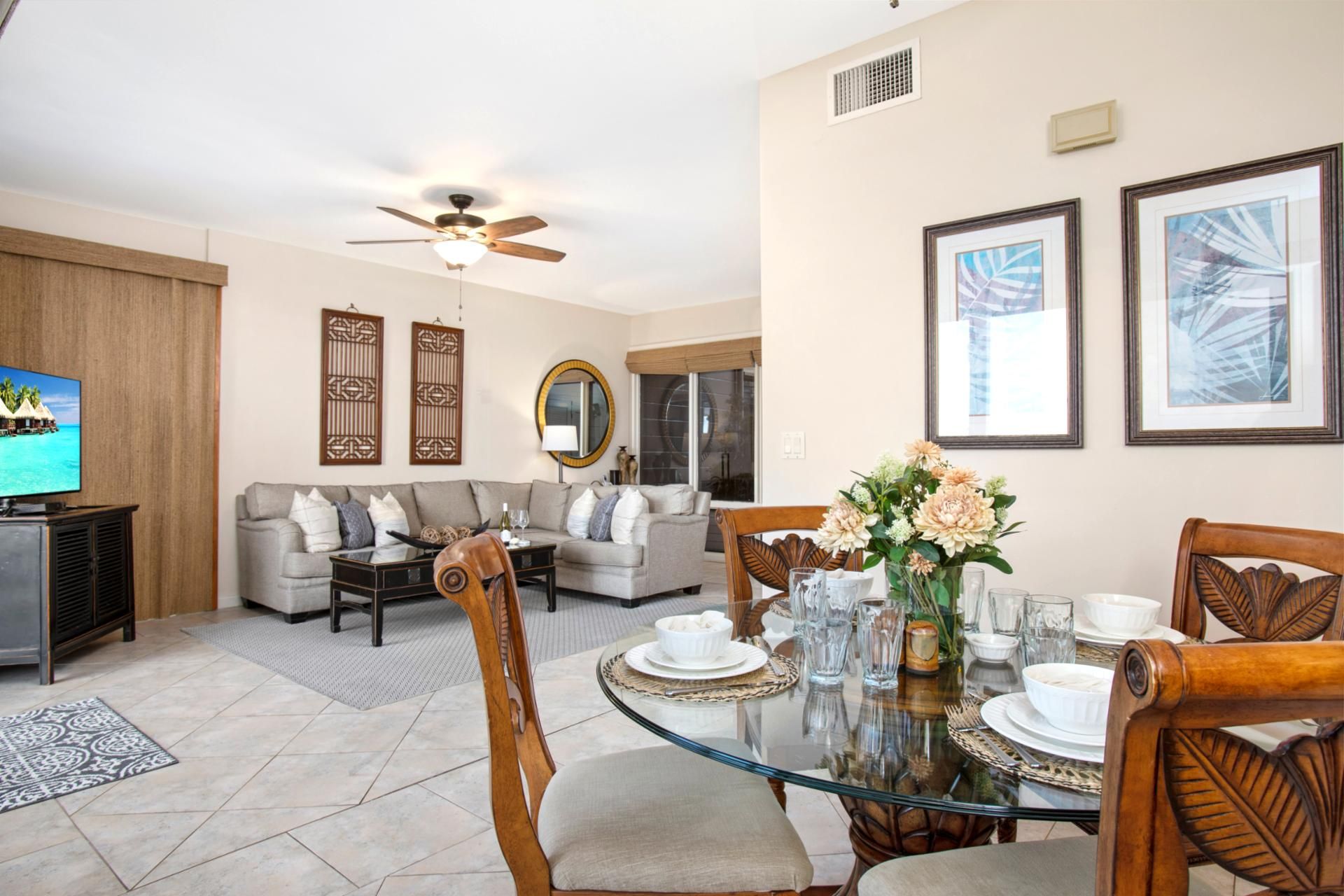 A modern living room with a glass dining table, a sofa, and a television.