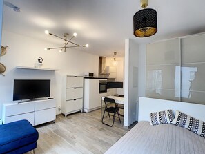 A modern bedroom with a bed, a desk, a chair, a television, and a kitchenette.