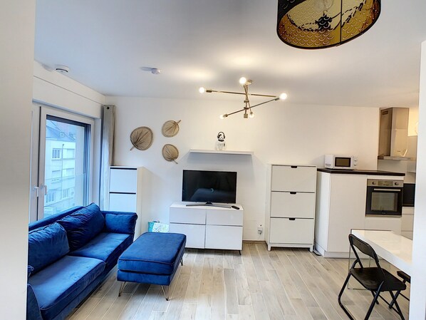 A modern living room with a blue sofa, a flat-screen TV, and a dining area with a small table and chairs.