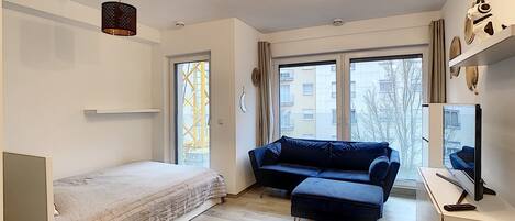 Une chambre moderne comprenant un lit, un bureau, une chaise, un canapé et une grande fenêtre donnant sur des immeubles.