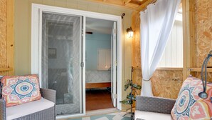 Une pièce meublée de meubles en osier, une porte-fenêtre coulissante donnant sur une chambre, et un luminaire fixé au mur.