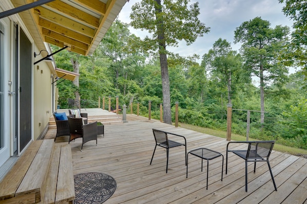 A wooden deck with outdoor furniture, including chairs and a table, overlooking a forested area.