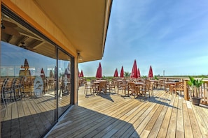 Une terrasse en bois avec des sièges extérieurs, des parasols rouges et une vue sur la plage.