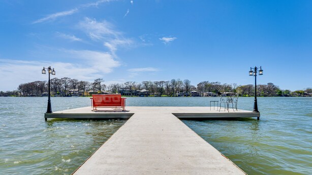 Een betonnen steiger die zich uitstrekt over een wateroppervlak, met een rode bank en twee lantaarnpalen aan beide zijden.