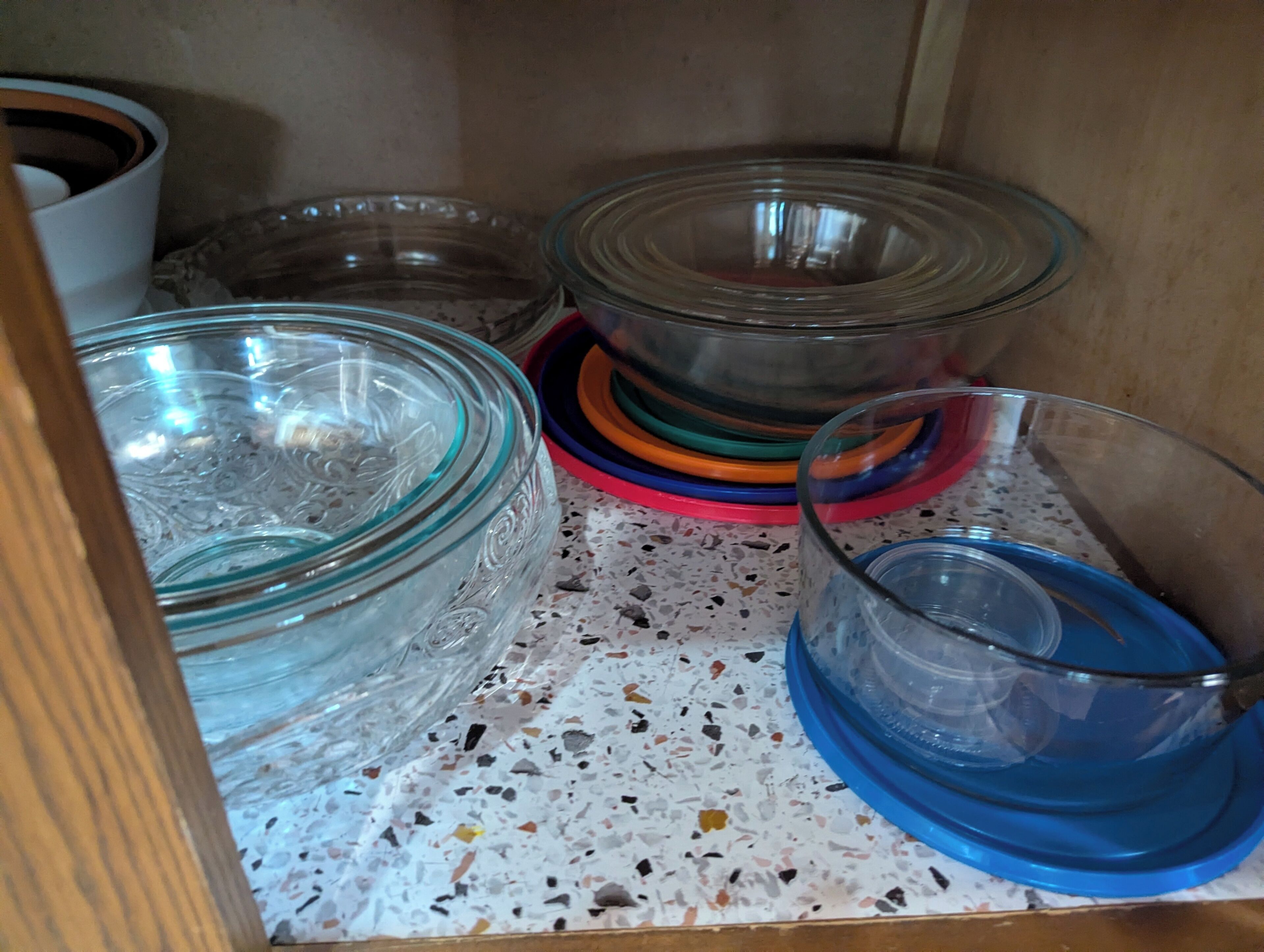 A kitchen cabinet with glass bowls and plates.