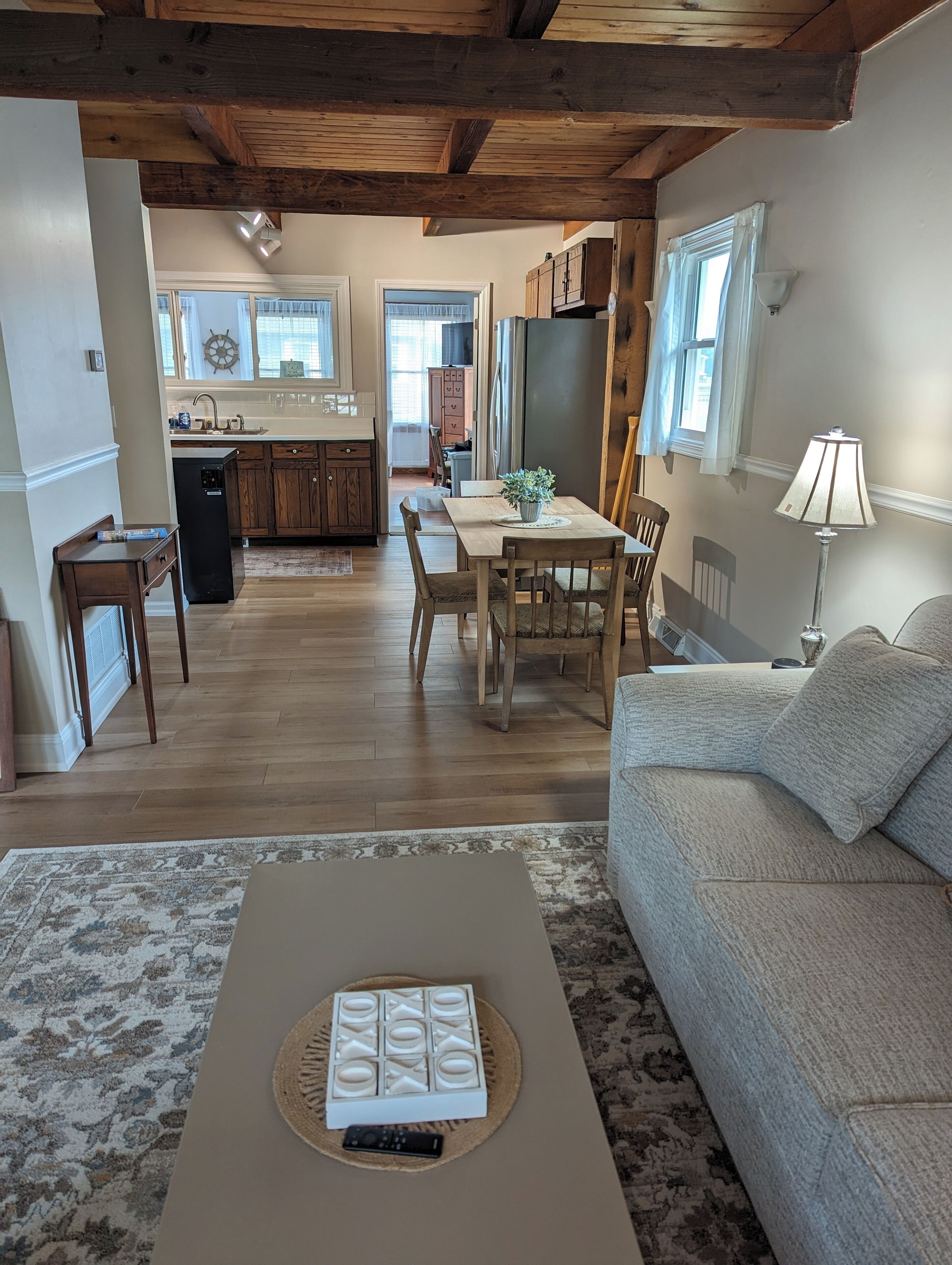 A spacious living area with a wooden ceiling, a dining table with chairs, a sofa, and a coffee table with a remote control.