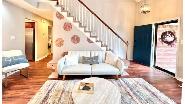 Una sala de estar moderna con una escalera, un conjunto de sofás y una mesa de centro redonda.