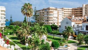 A resort area with multiple buildings, including a large multi-story structure with balconies and a smaller building with a tiled roof. There are palm trees and well-maintained lawns.