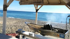 A beachside restaurant named 'Playa Botavara' with a thatched roof, a boat with cooking equipment, and a view of the sea.