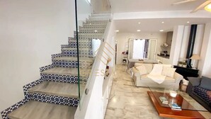 A spacious living area with a staircase featuring patterned tiles, a sofa set, and a coffee table.