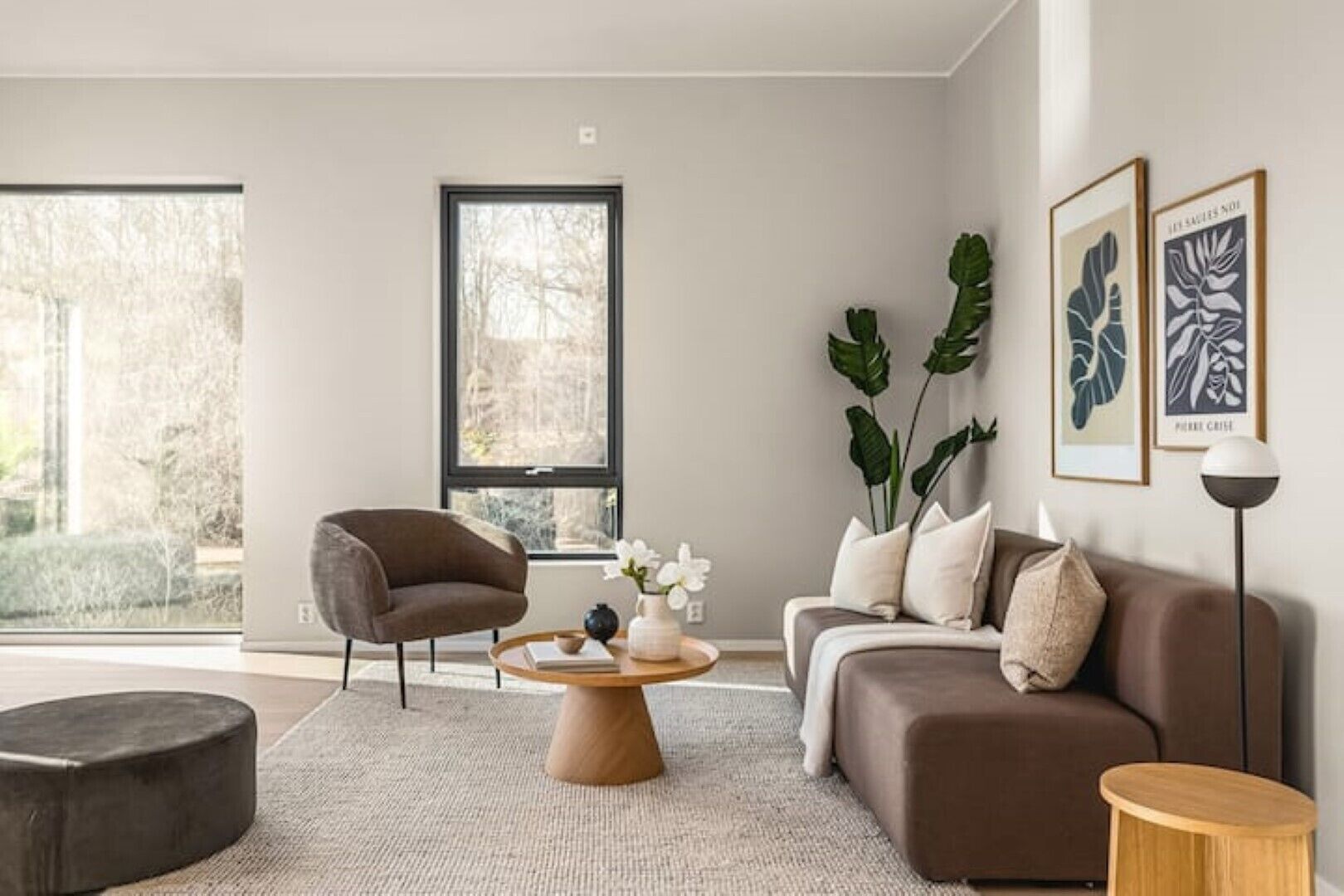 A modern living room with a sofa, armchair, coffee table, and large windows.