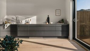 Eine moderne Küche mit großem Fenster, dunklen Schränken und Holzboden.