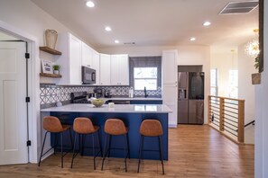 A modern kitchen with white cabinets, a blue island with bar stools, and wooden flooring.