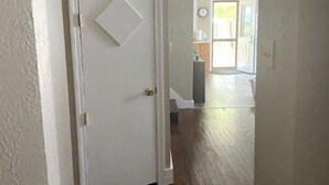 Un pasillo con una puerta blanca, suelo de madera y vistas a una habitación con ventana y un reloj en la pared.