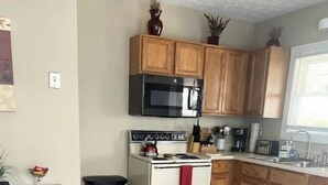 Una cocina con armarios de madera, estufa, microondas y pileta.