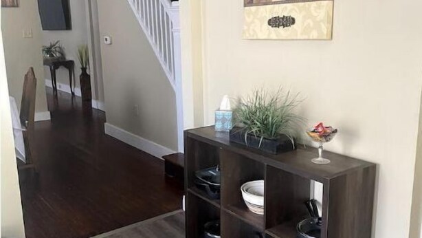 Un pasillo con piso de madera oscura, una consola con utensilios de cocina, una escalera y un elemento decorativo en la pared.