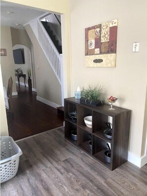 A hallway with a dark wood floor, a console table with kitchenware, a staircase, and a decorative wall piece. - The Townhouse in Dayton- Close to UD (Dayton)