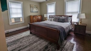 Un dormitorio con cama de madera, ventilador de techo y ventana grande con persianas.