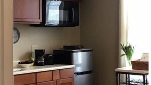 Uma cozinha compacta com armários de madeira, um micro-ondas preto e uma geladeira de aço inoxidável.