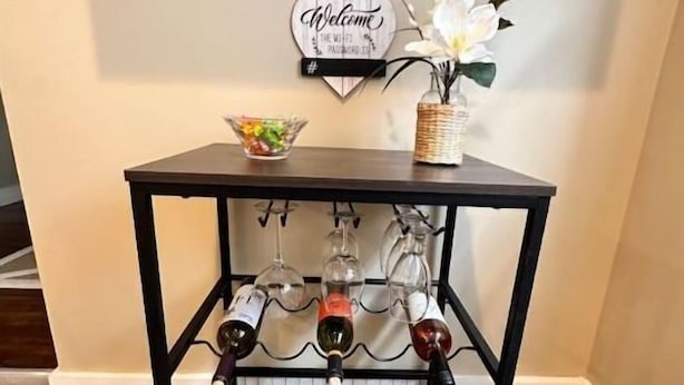 Et sort metalbord med et vinrack, en skål med snacks og et velkommenskilt på væggen bagved.