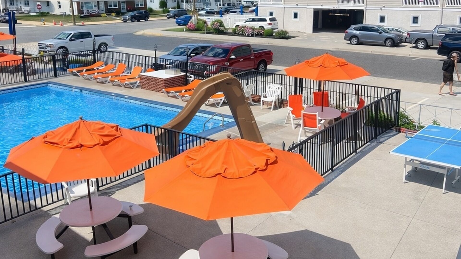A poolside area with orange umbrellas, lounge chairs, and a ping pong table.