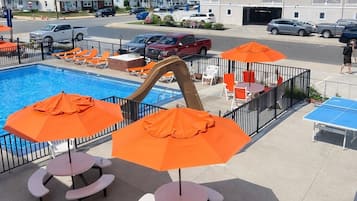 A poolside area with orange umbrellas, lounge chairs, and a ping pong table.