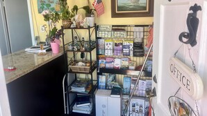 A reception area with a counter, shelves with brochures, a painting of a ship, and a door labeled "OFFICE". - Sea Chest Motel  (Wildwood Crest)