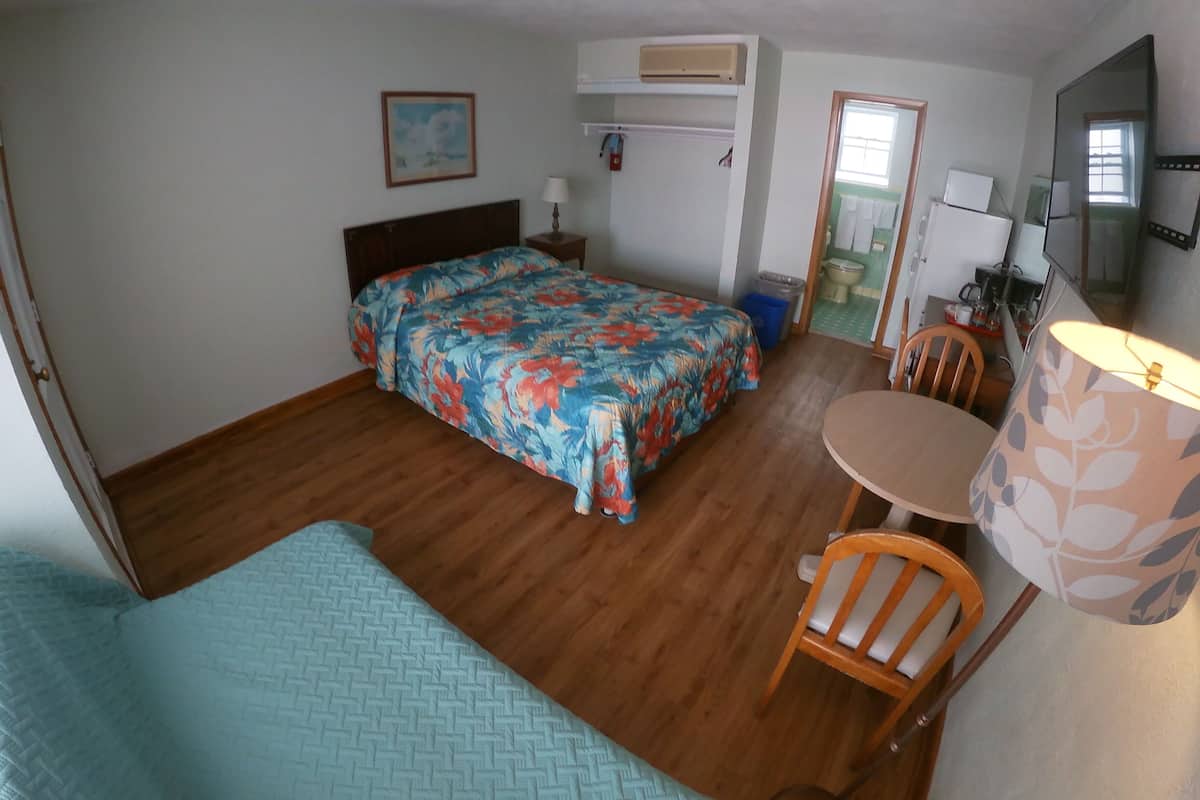 Une chambre à coucher avec un lit, une chaise, une petite table et une salle de bain visible à travers une porte ouverte.