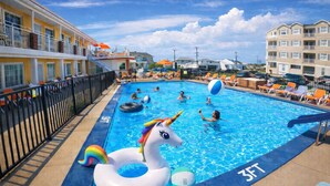 A swimming pool with a unicorn float, lounge chairs, and a building with balconies. - Sea Chest Motel  (Wildwood Crest)