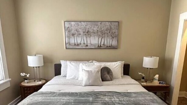 A bedroom with a large bed, two bedside tables, a painting on the wall, and a window. - Farmhouse in the City (Dayton)