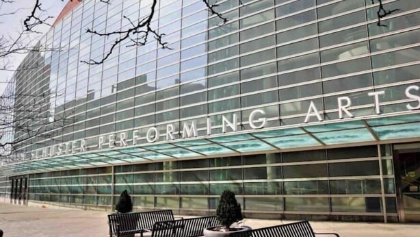 Un bâtiment moderne avec une façade en verre sur laquelle on peut lire les mots « SCHUSTER PERFORMING ARTS ».